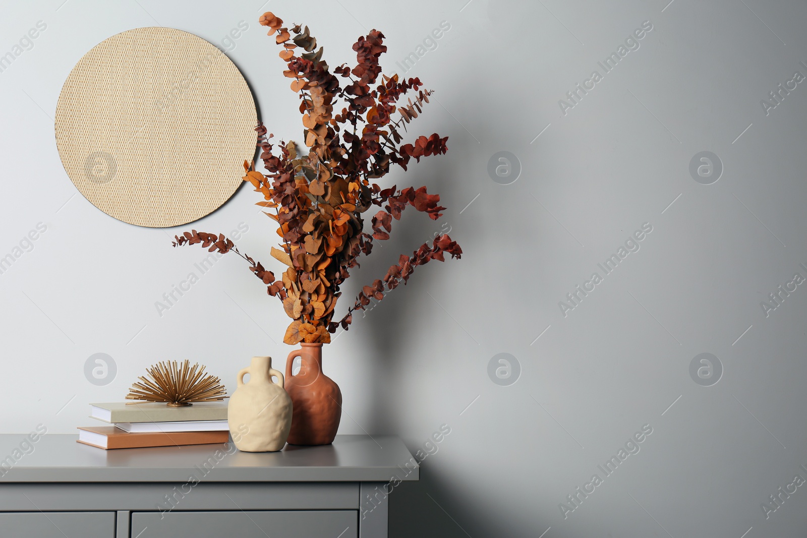 Photo of Stylish vases, dried eucalyptus branches and books on grey table near white wall indoors, space for text. Interior design