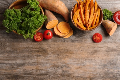 Photo of Flat lay composition with bowl of sweet potato fries on wooden background. Space for text