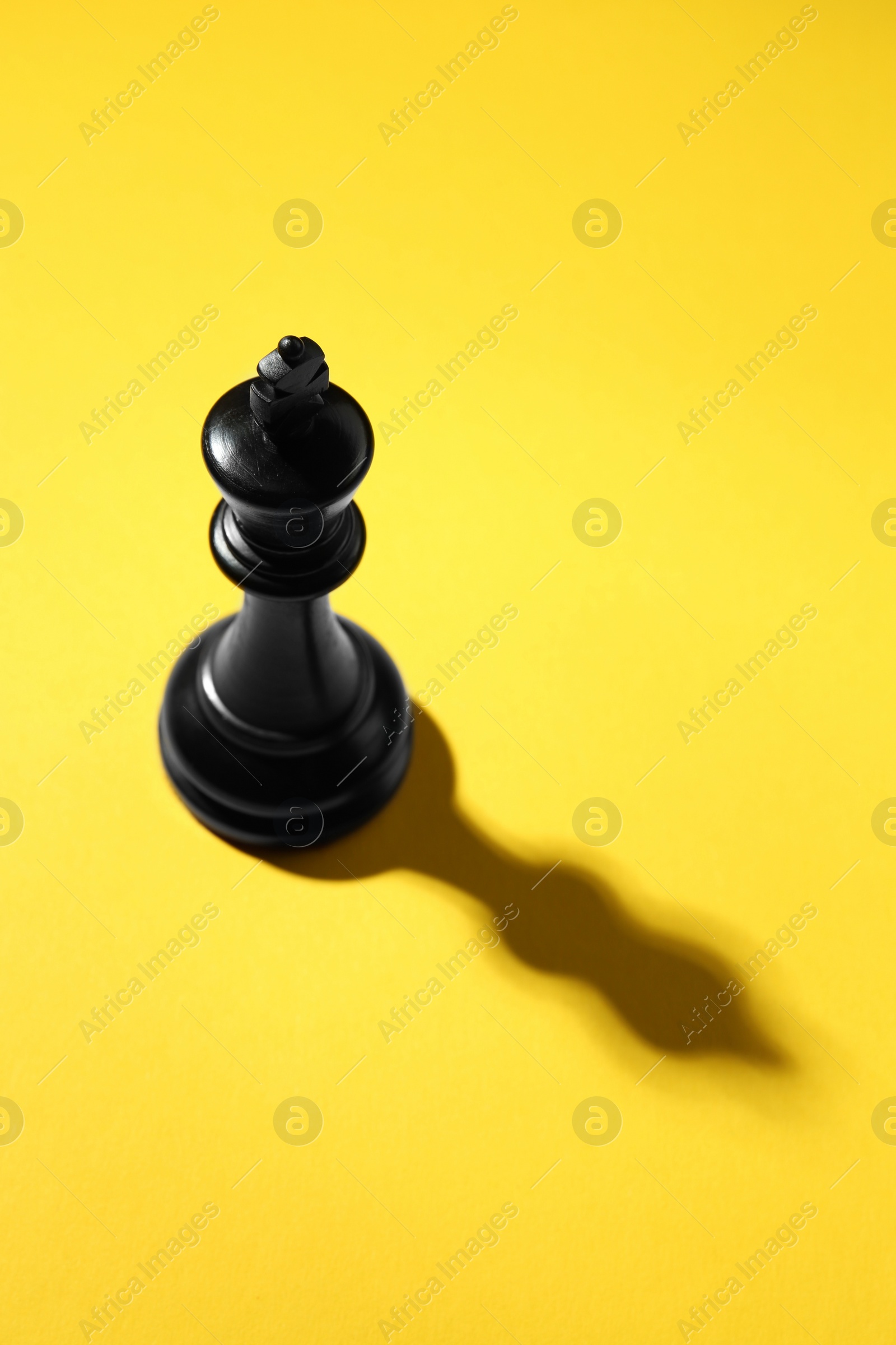 Photo of Black wooden chess king on yellow background, above view