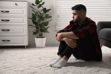 Photo of Sad man sitting on floor at home. Space for text