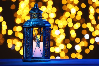 Traditional Arabic lantern on table against blurred lights at night. Space for text