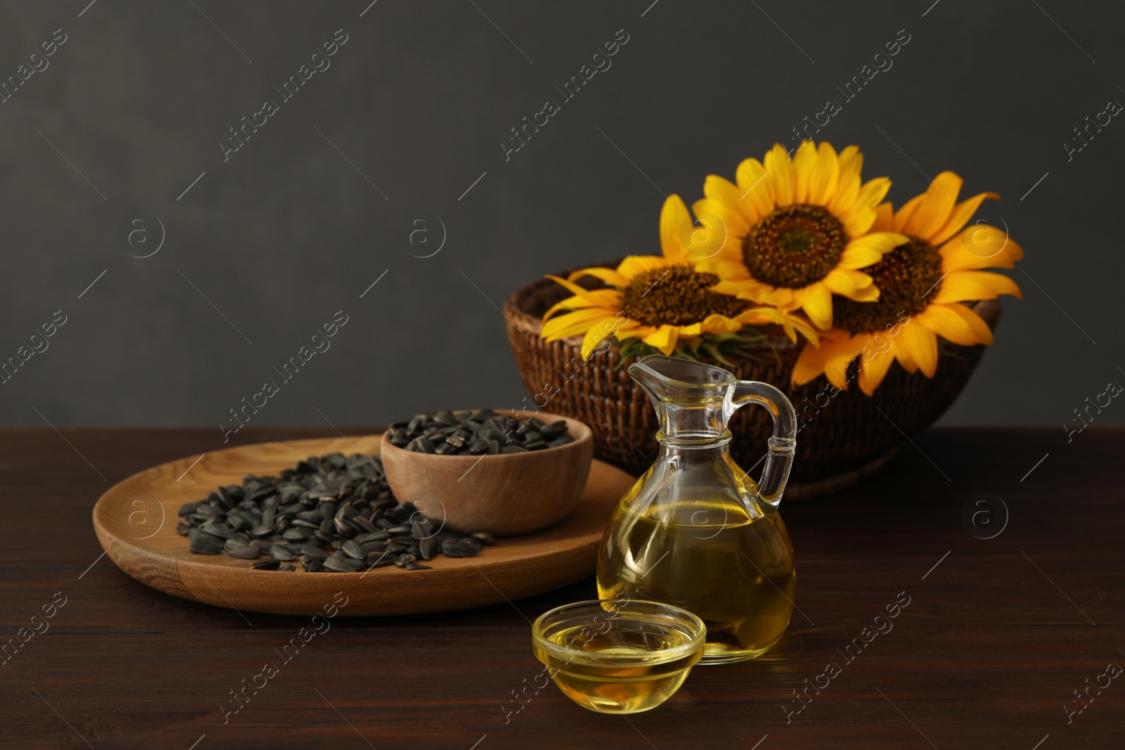 Photo of Sunflower oil and seeds on wooden table against grey background