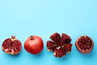Photo of Whole and cut fresh pomegranates on light blue background, flat lay. Space for text