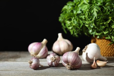 Photo of Fresh raw garlic and parsley on wooden table against black background, closeup. Space for text