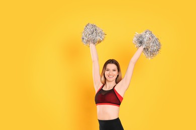 Photo of Beautiful cheerleader in costume holding pom poms on yellow background. Space for text
