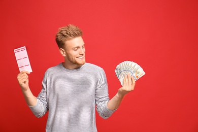 Photo of Portrait of happy young man with money fan and lottery ticket on red background