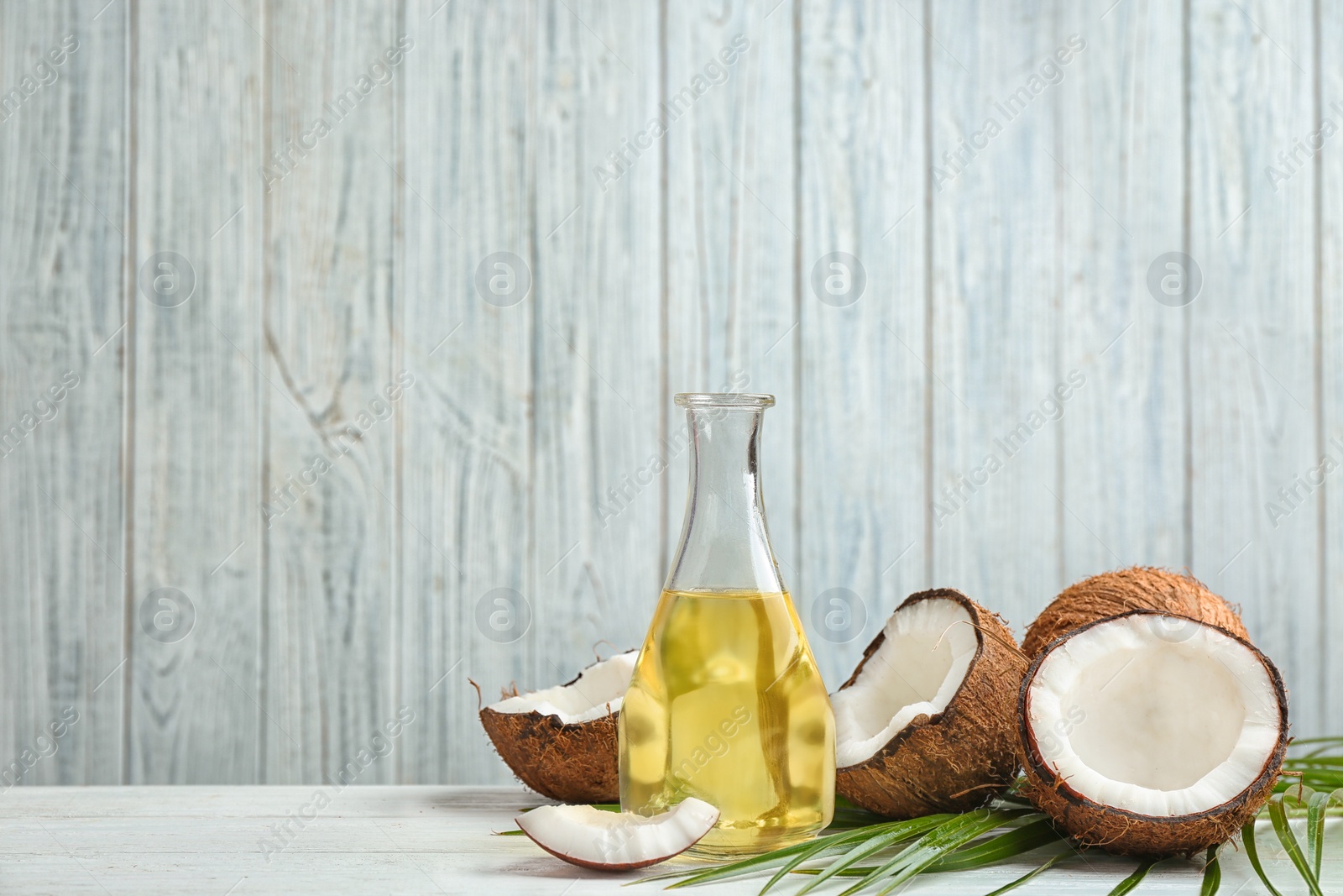 Photo of Bottle of natural organic oil and coconuts on white wooden table. Space for text