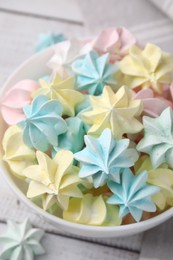 Tasty meringue cookies in bowl on white wooden table