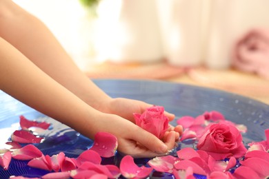 Photo of Child holding rose flower in bowl with water and petals on blurred background, closeup. Space for text