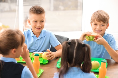 Photo of Happy children at table with healthy food in school canteen