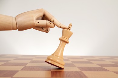 Robot touching chess piece on board against light background. Wooden hand representing artificial intelligence