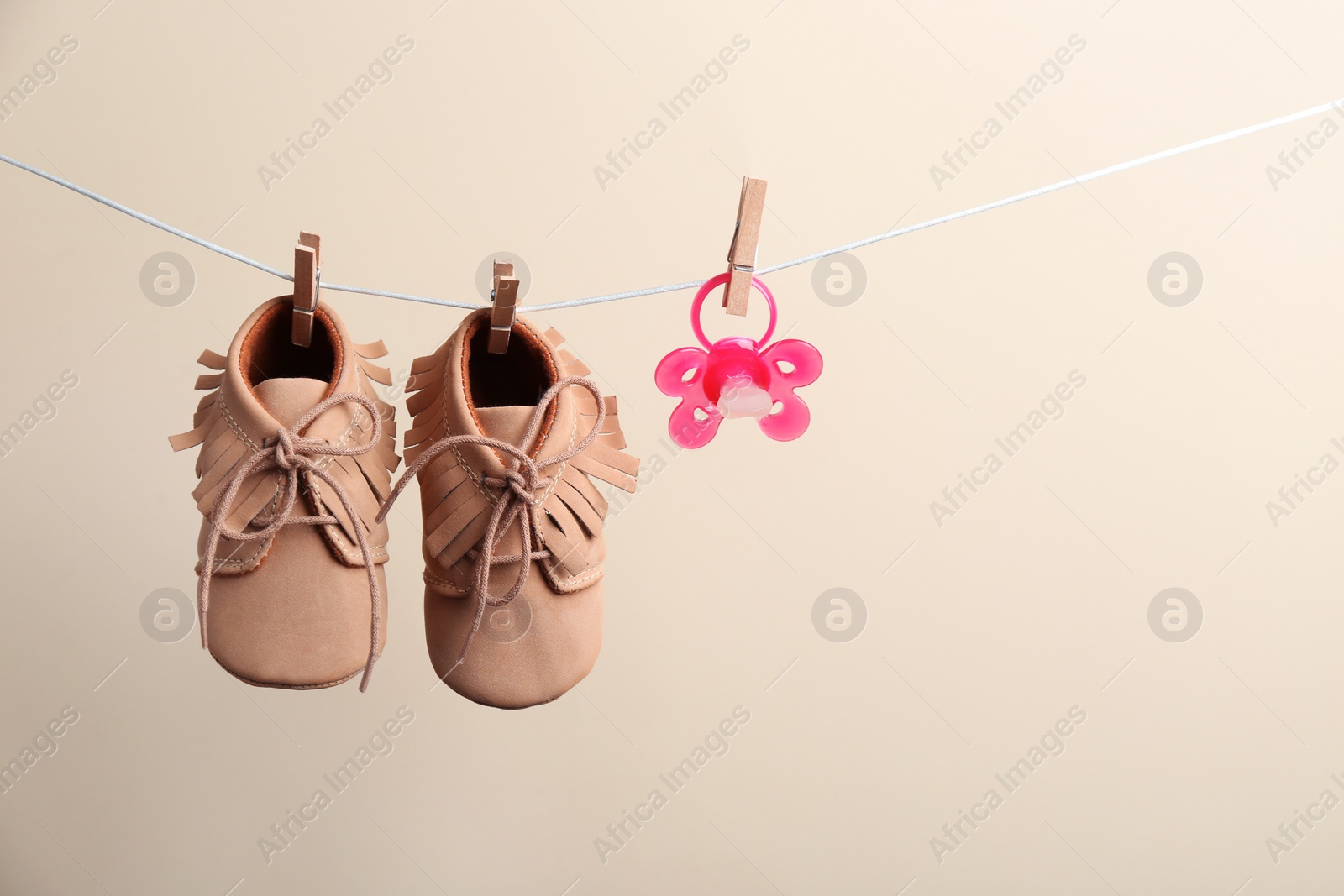 Photo of Small shoes and pacifier hanging on washing line against color background, space for text. Baby accessories