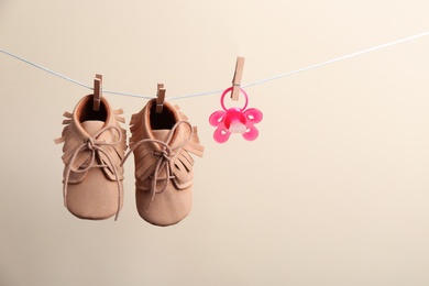 Small shoes and pacifier hanging on washing line against color background, space for text. Baby accessories