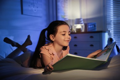 Little girl reading fairy tale in dark bedroom