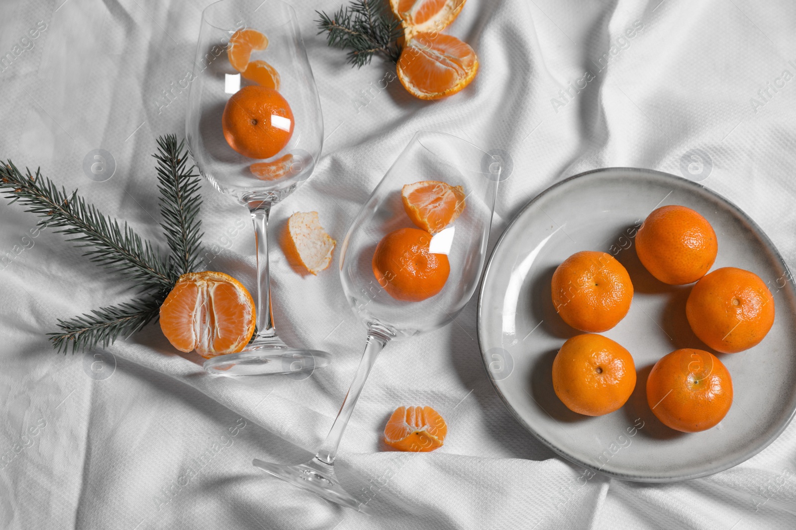 Photo of Delicious fresh ripe tangerines and glasses on white bedsheet, flat lay