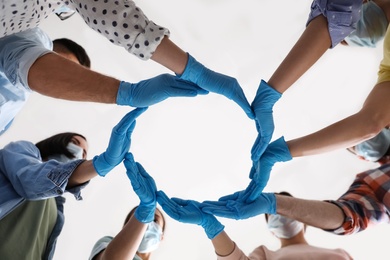 Photo of People in blue medical gloves showing circle with hands on light background, low angle view