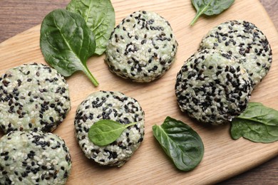 Photo of Tasty vegan cutlets with sesame seeds and spinach on wooden board, top view