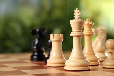 Photo of White wooden king and other chess pieces on game board against blurred background, closeup. Space for text