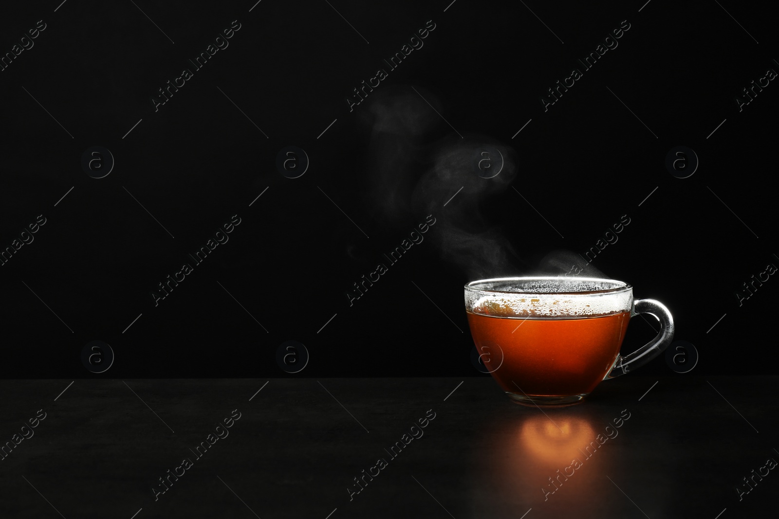 Photo of Glass cup of hot tea on table against black background, space for text