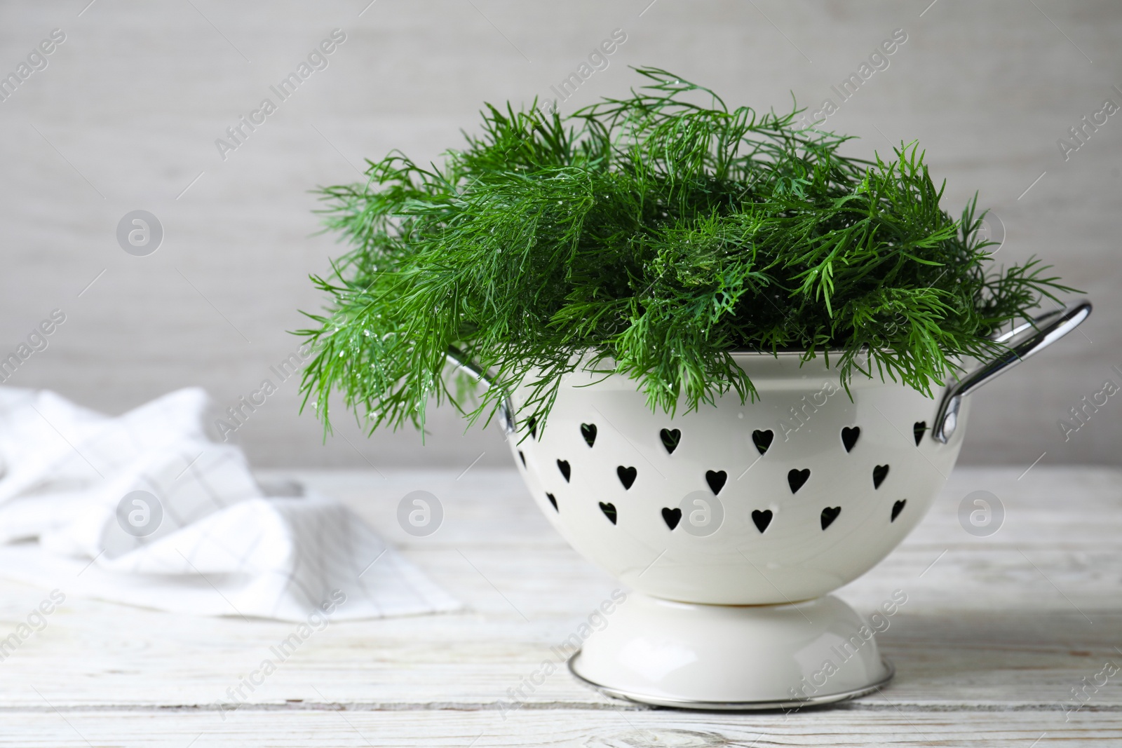 Photo of Fresh dill in colander on white wooden table