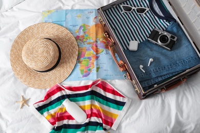 Suitcase with clothes and travel accessories on white fabric, above view. Summer vacation