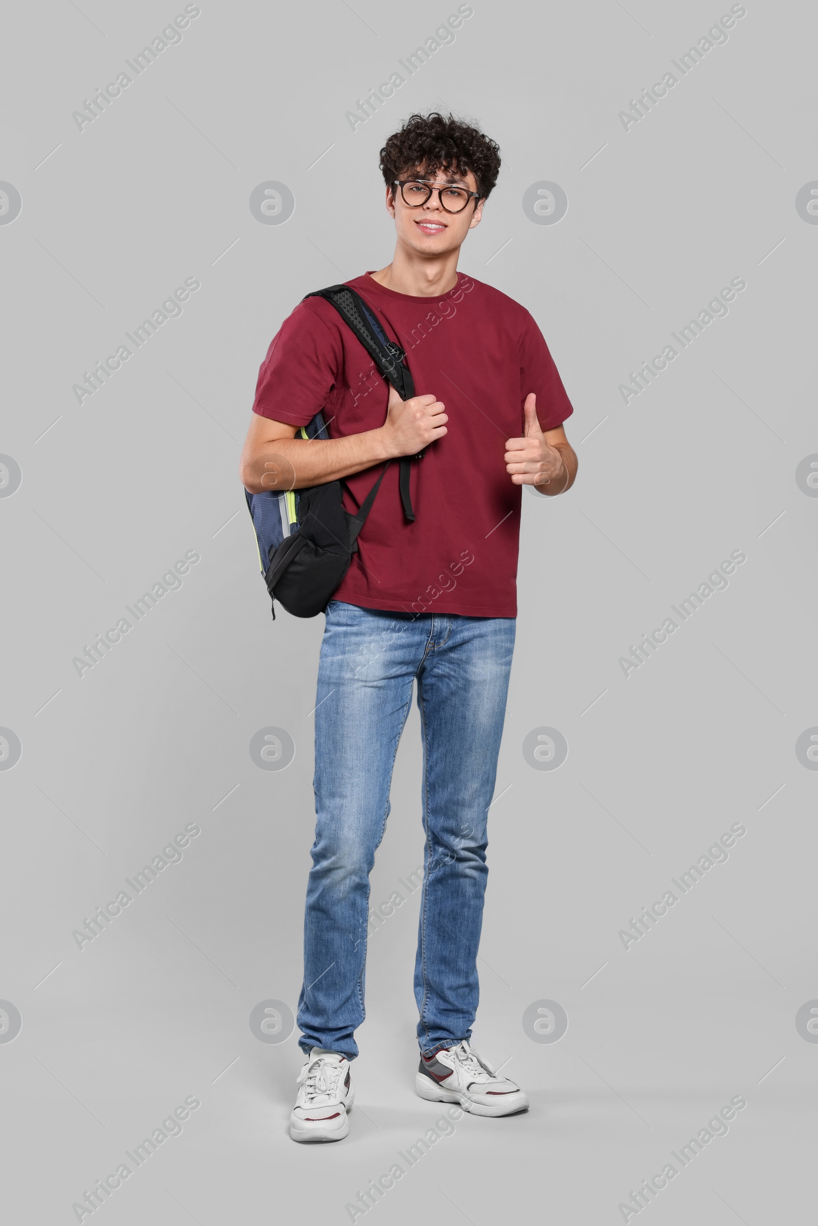 Photo of Handsome young man with backpack showing thumb up on light grey background