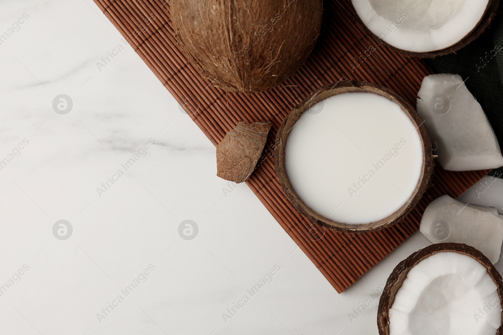 Photo of Delicious vegan milk in coconut and pieces of ripe fruit on white marble table, flat lay. Space for text
