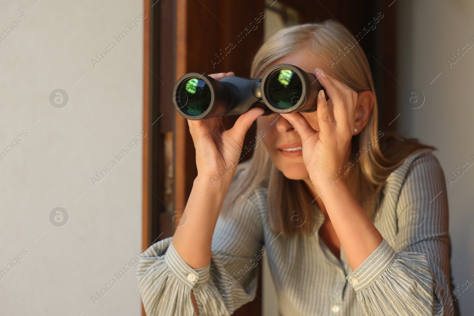 Photo of Concept of private life. Curious senior woman with binoculars spying on neighbours outdoors