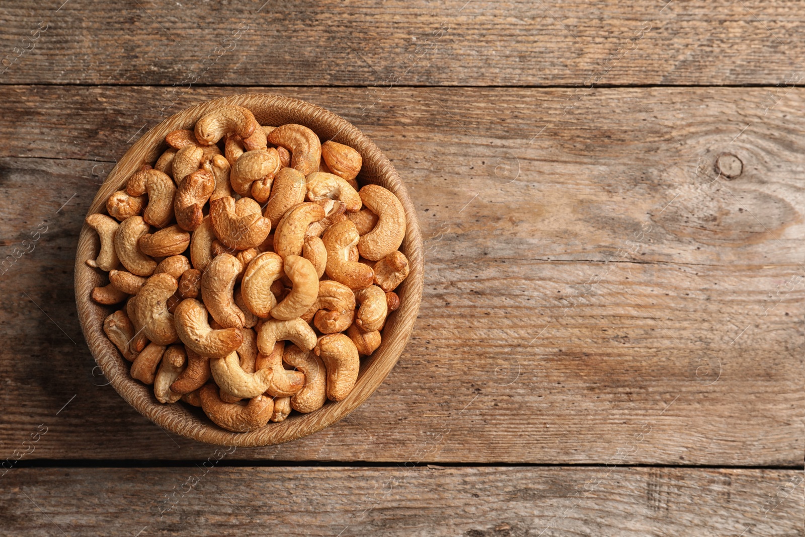 Photo of Tasty cashew nuts in bowl on wooden table, top view. Space for text