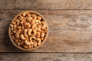 Photo of Tasty cashew nuts in bowl on wooden table, top view. Space for text