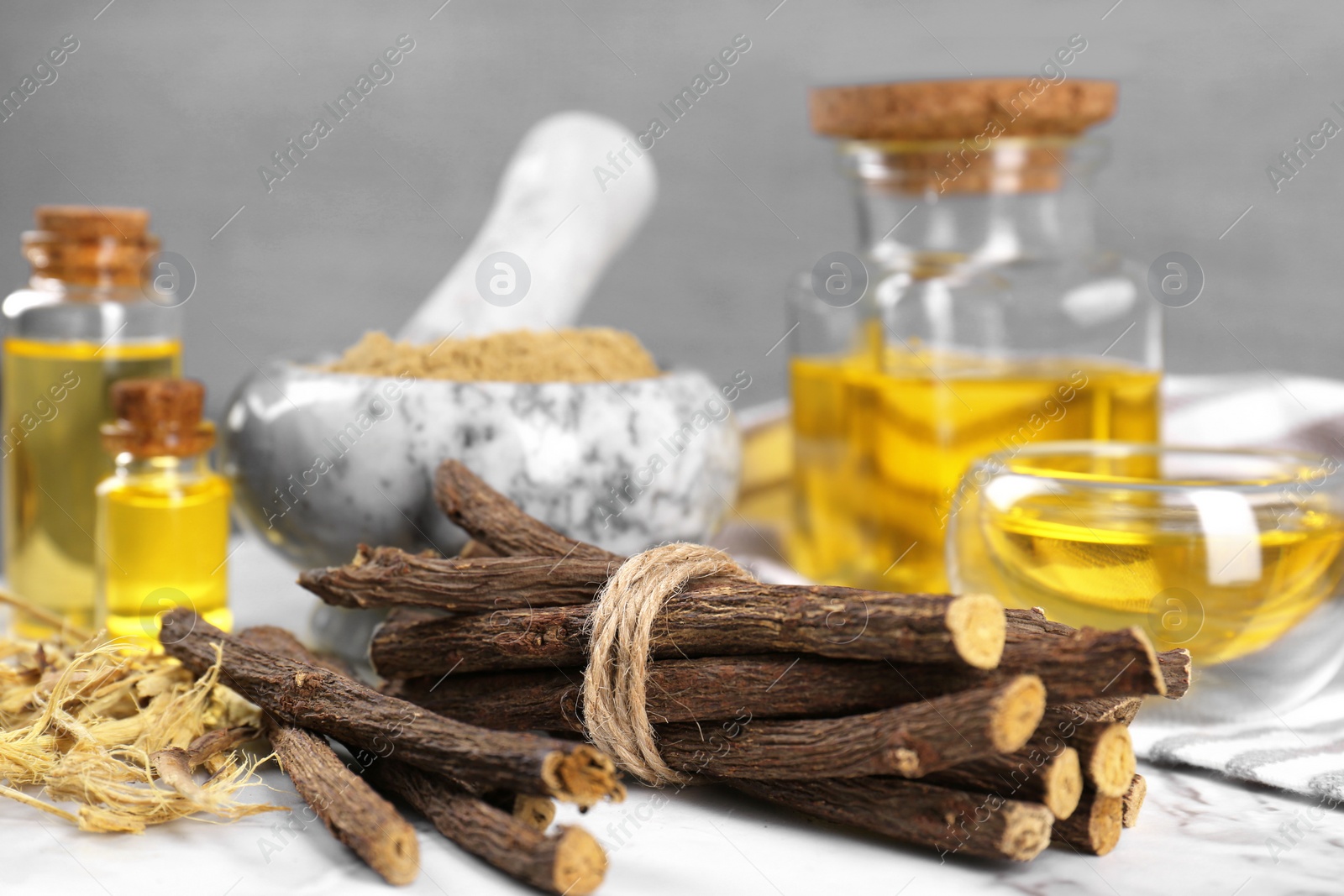 Photo of Dried sticks of licorice roots, shavings and essential oil on white table, closeup