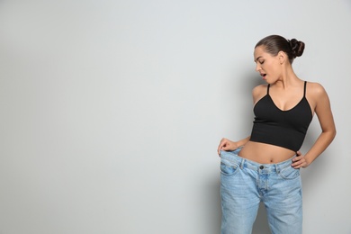 Photo of Slim woman in oversized jeans on light background, space for text. Weight loss