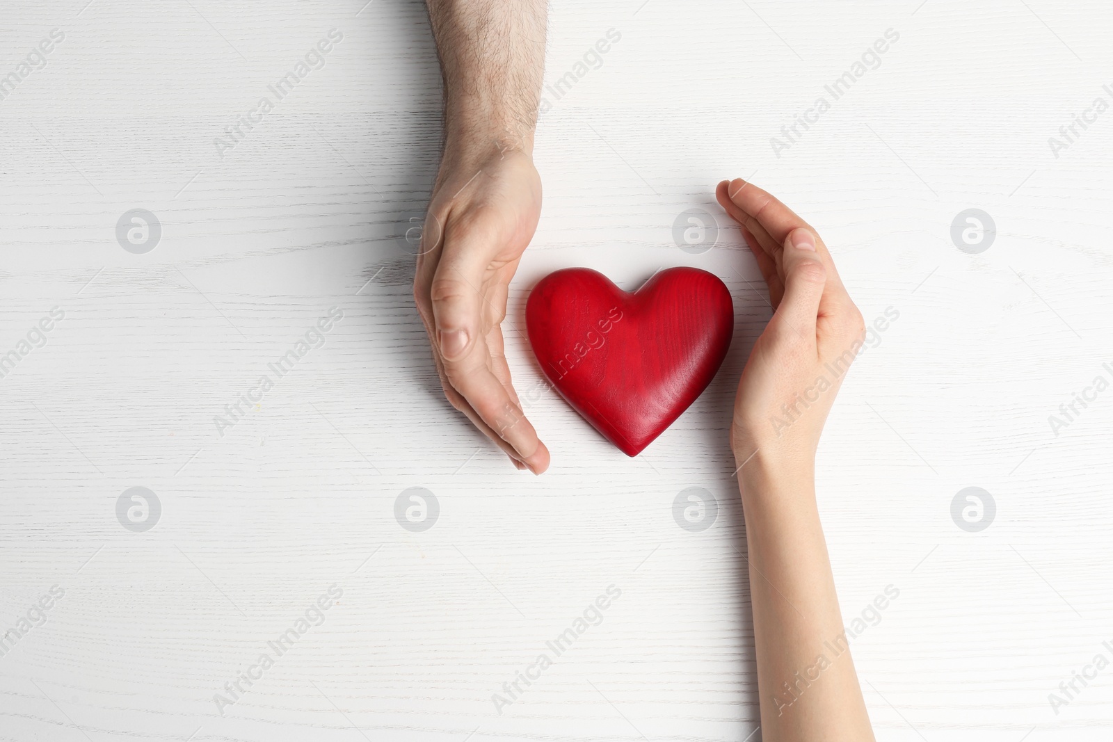 Photo of Couple holding decorative heart on white wooden background, top view
