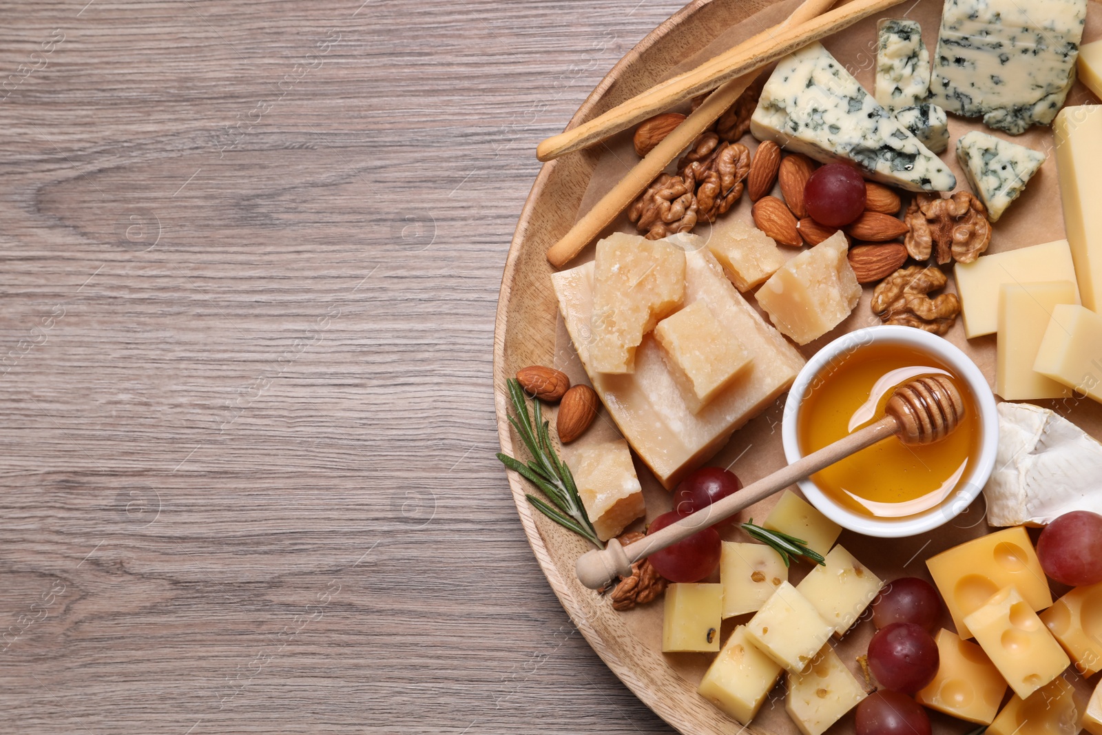 Photo of Cheese plate with honey, grapes and nuts on wooden table, top view. Space for text