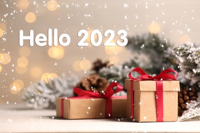 Image of Hello 2023. Gift boxes and Christmas decor on wooden table against blurred festive lights