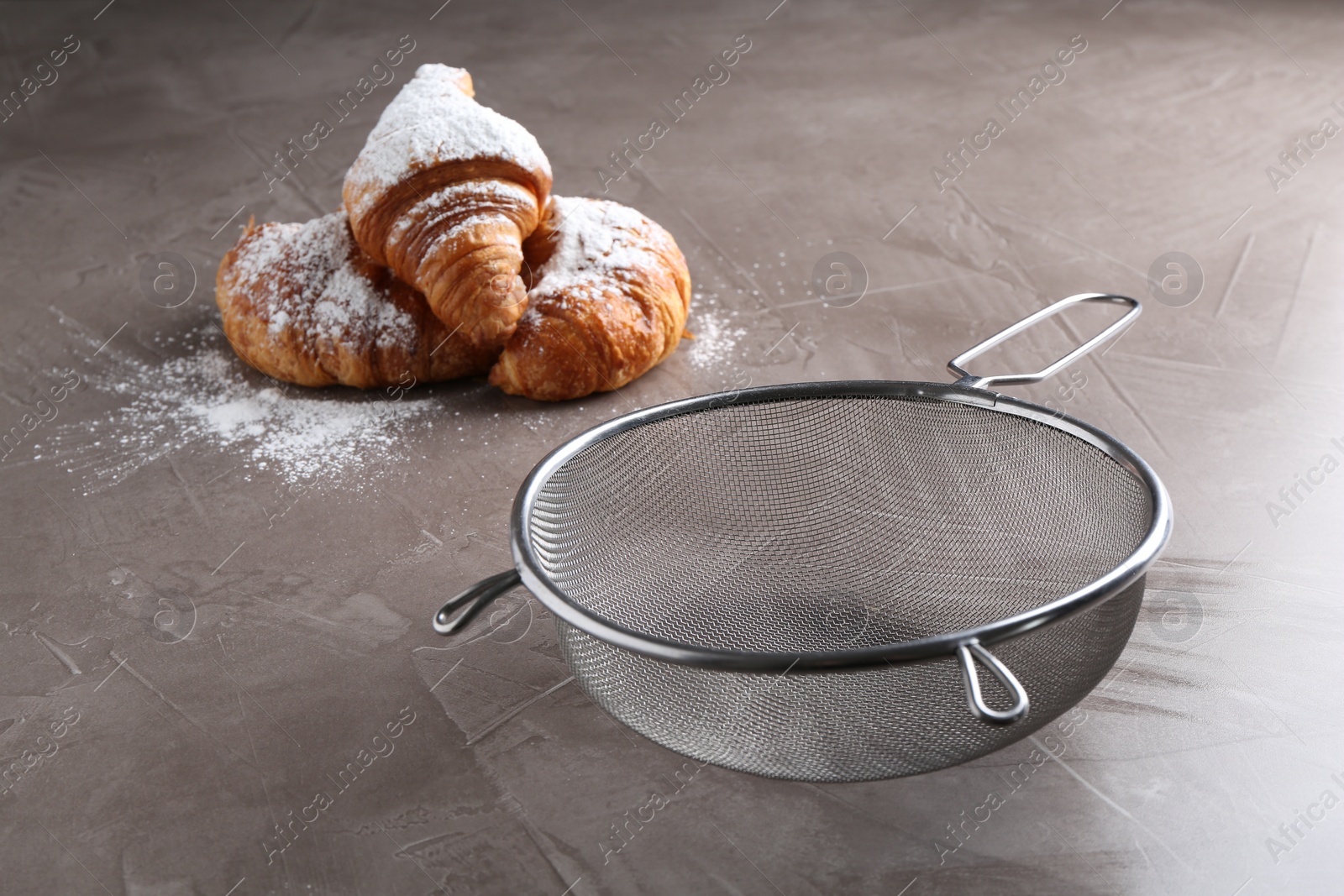 Photo of Clean sieve and croissants with sugar powder on grey textured table