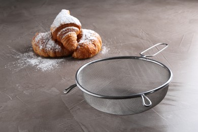 Clean sieve and croissants with sugar powder on grey textured table