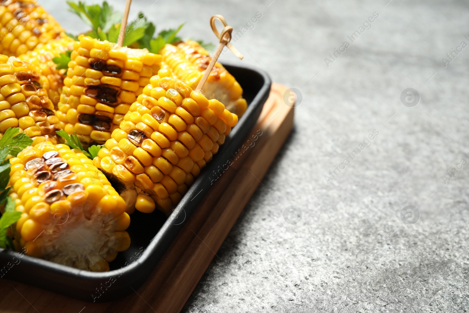 Photo of Tasty grilled corn on grey table, closeup.  Space for text