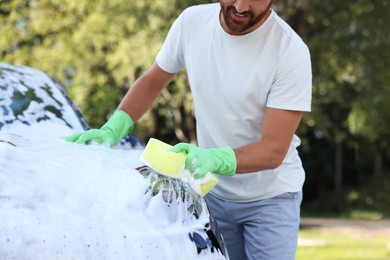 Photo of Man washing car with sponge outdoors, closeup