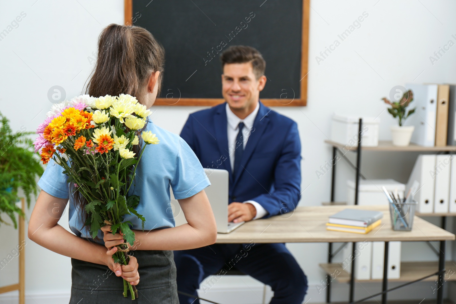 Photo of Schoolgirl with bouquet congratulating her pedagogue in classroom. Teacher's day