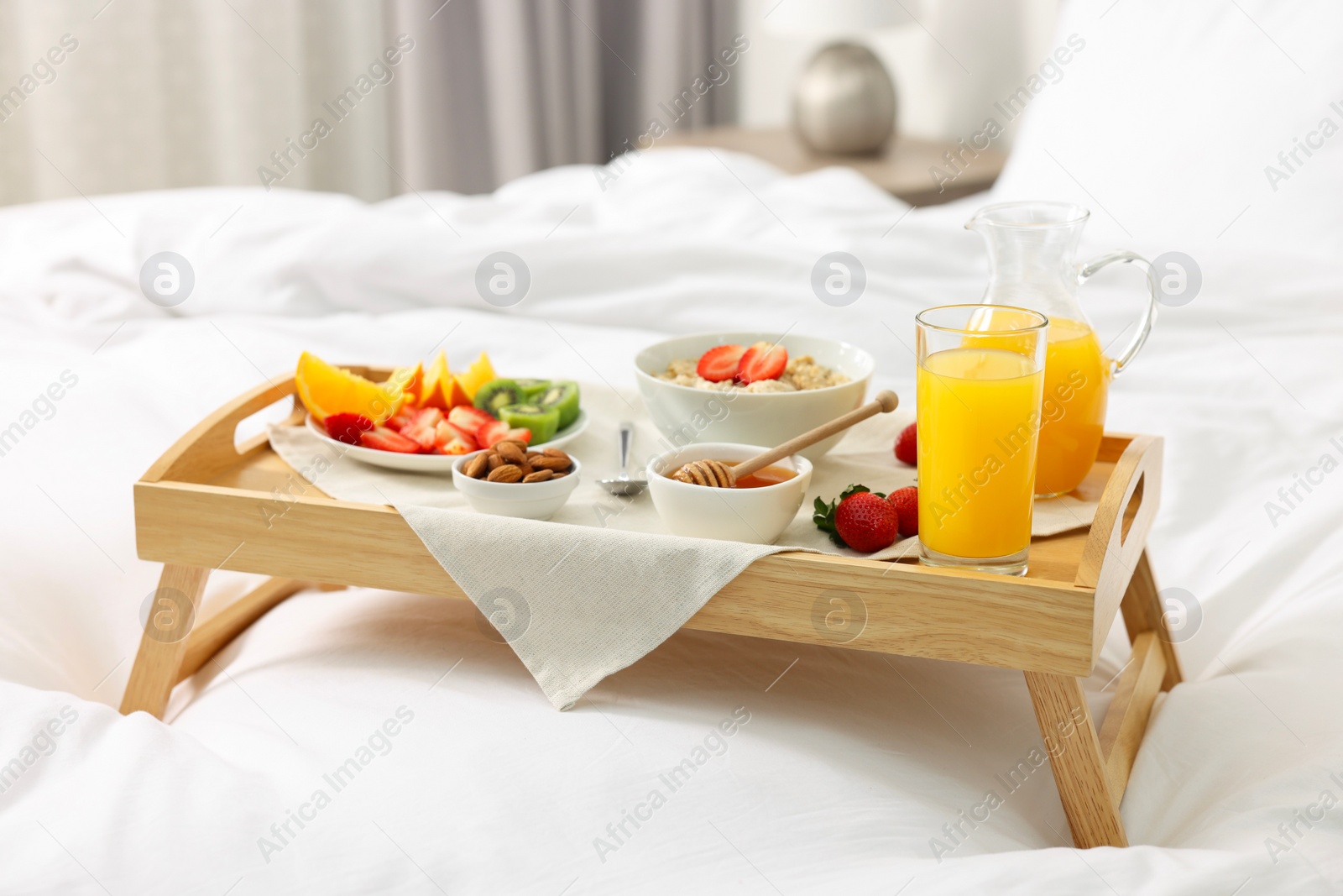 Tasty breakfast served in bed. Oatmeal, juice, fruits, almonds and honey on wooden tray Photo of Tasty breakfast served in bed. Oatmeal, juice, fruits, almonds and honey on wooden tray