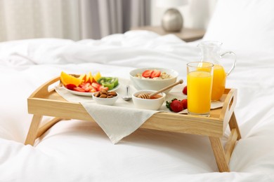 Photo of Tasty breakfast served in bed. Oatmeal, juice, fruits, almonds and honey on wooden tray