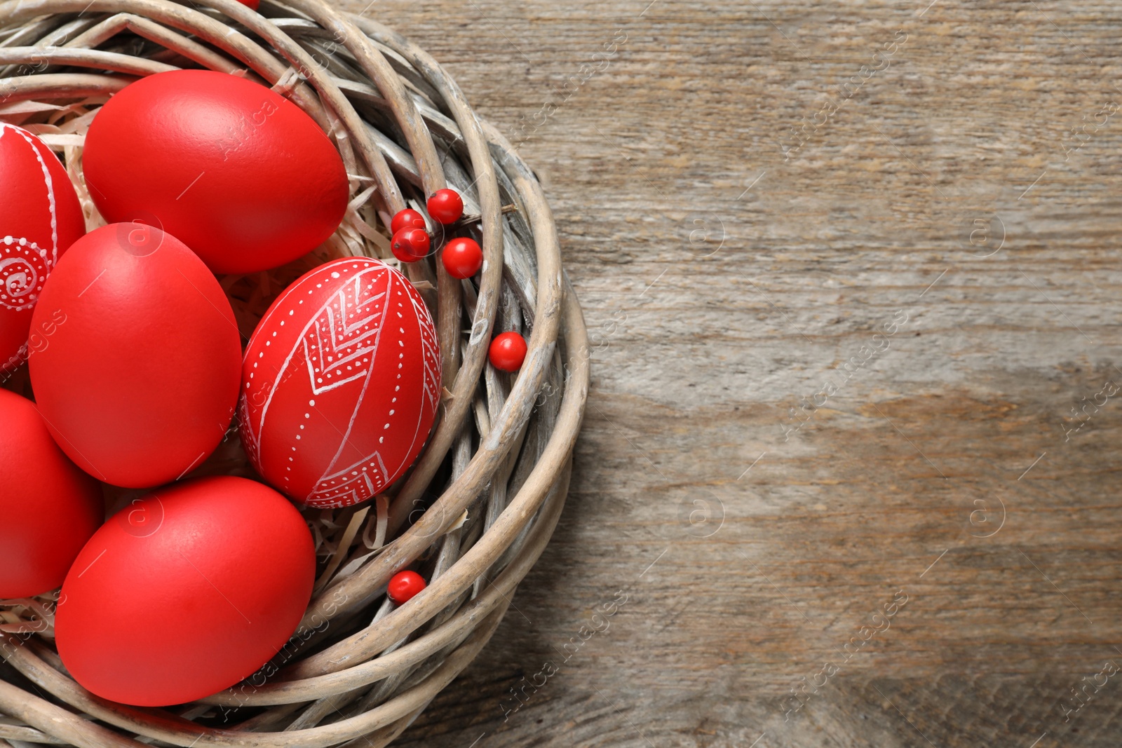 Photo of Wicker nest with painted Easter eggs on wooden table, top view. Space for text