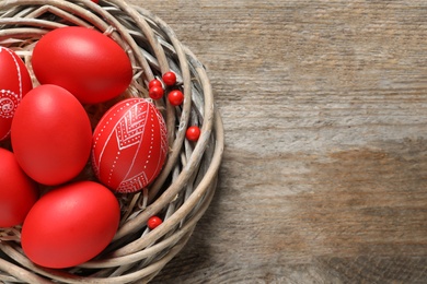 Wicker nest with painted Easter eggs on wooden table, top view. Space for text