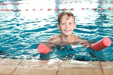 Photo of Little boy with swimming noodle in indoor pool