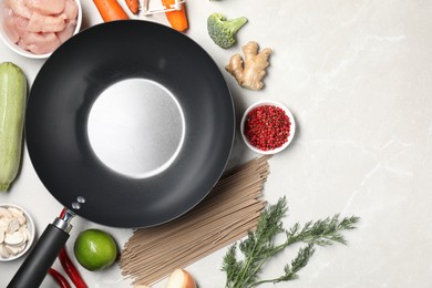 Photo of Empty iron wok surrounded by raw ingredients on light table, flat lay. Space for text