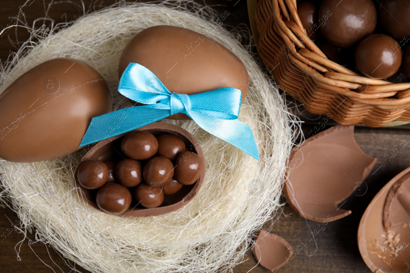 Photo of Tasty chocolate eggs with candies in decorative nest on wooden table, flat lay