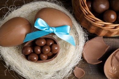 Tasty chocolate eggs with candies in decorative nest on wooden table, flat lay