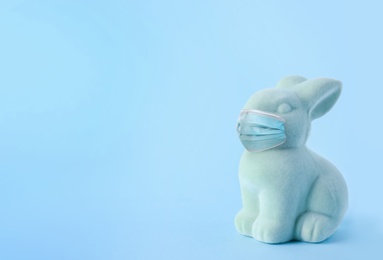 COVID-19 pandemic. Easter bunny toy in protective mask on light blue background, space for text 