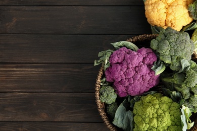 Photo of Wicker basket with different cabbages on wooden table, top view. Healthy food